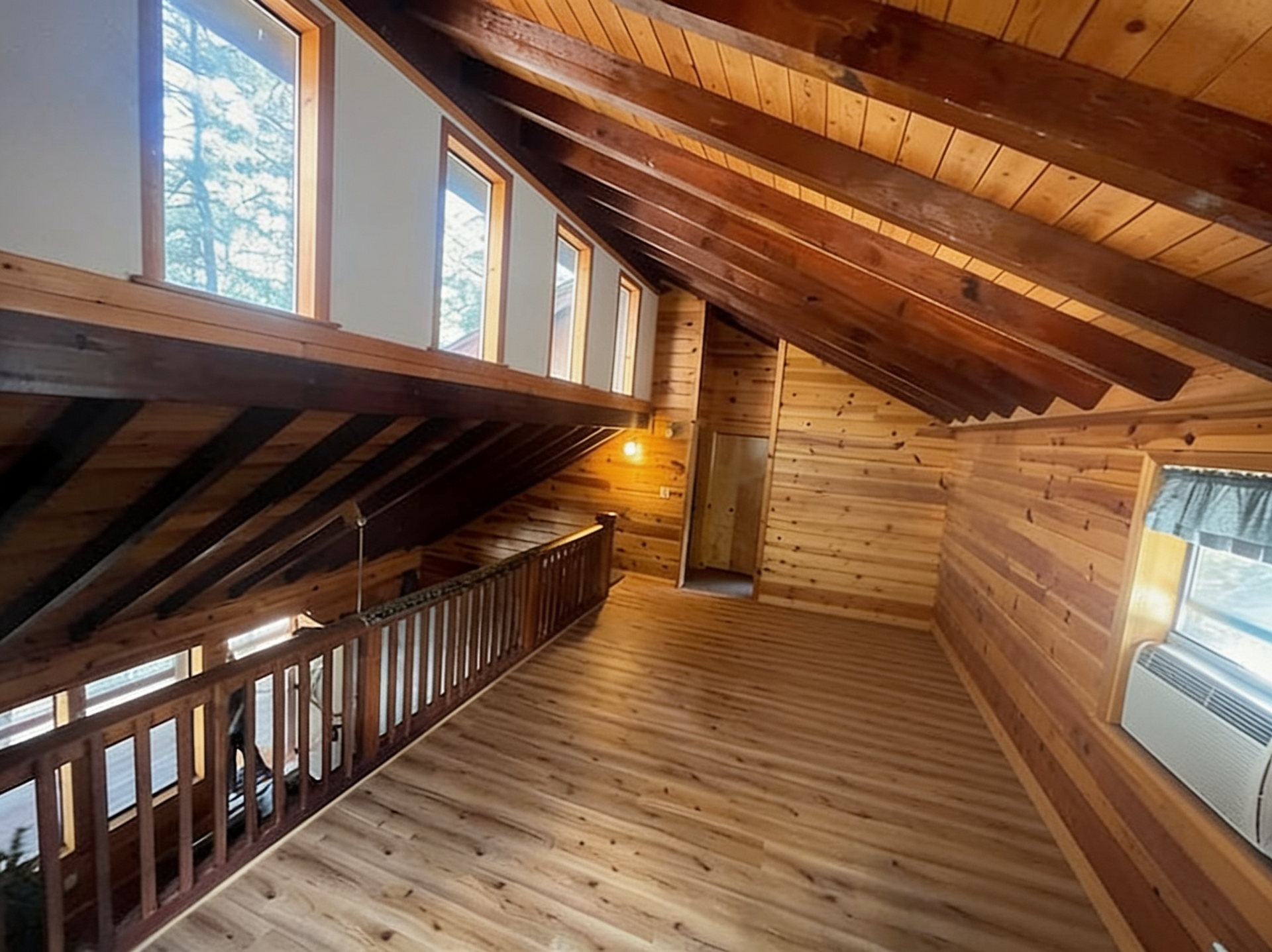 Empty wooden loft with sloped ceiling, railing, windows, and a wall-mounted heater