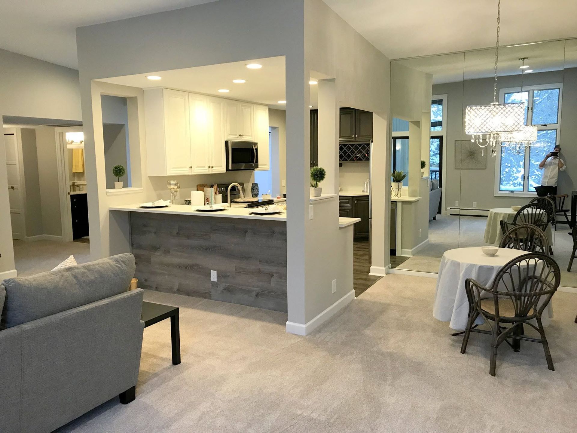Open-concept living room and kitchen with gray sofa, marble island, and small dining area near a bright window.