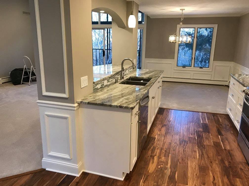 Open kitchen and living area with granite island, hardwood floors, white cabinets, and large windows