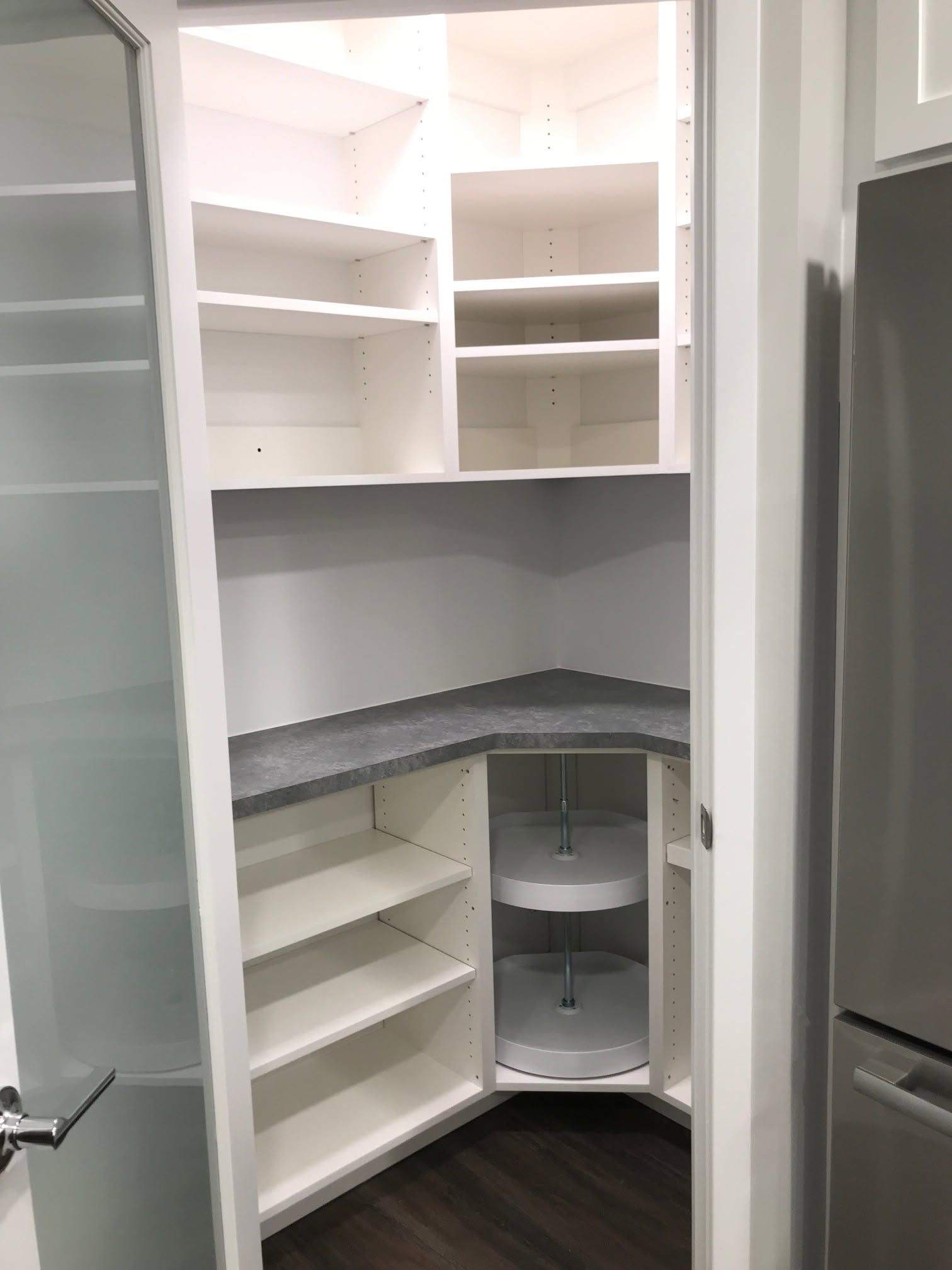 Built-in white corner pantry with shelves, gray countertop, and lower pull-out storage bins