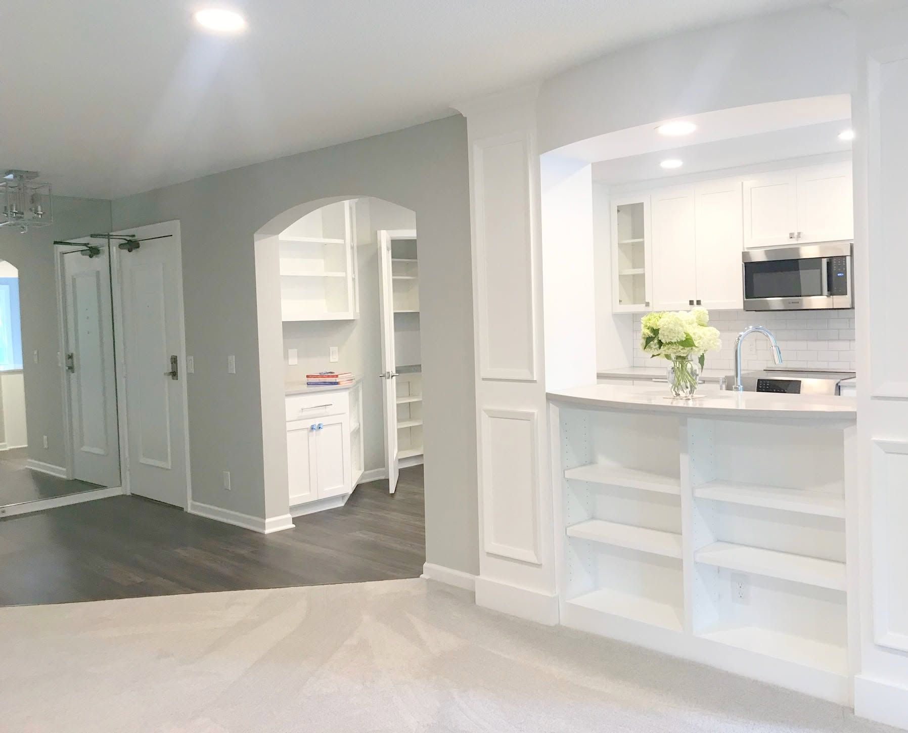 Bright open-concept kitchen and living area with white cabinetry, gray walls, and dark wood floors