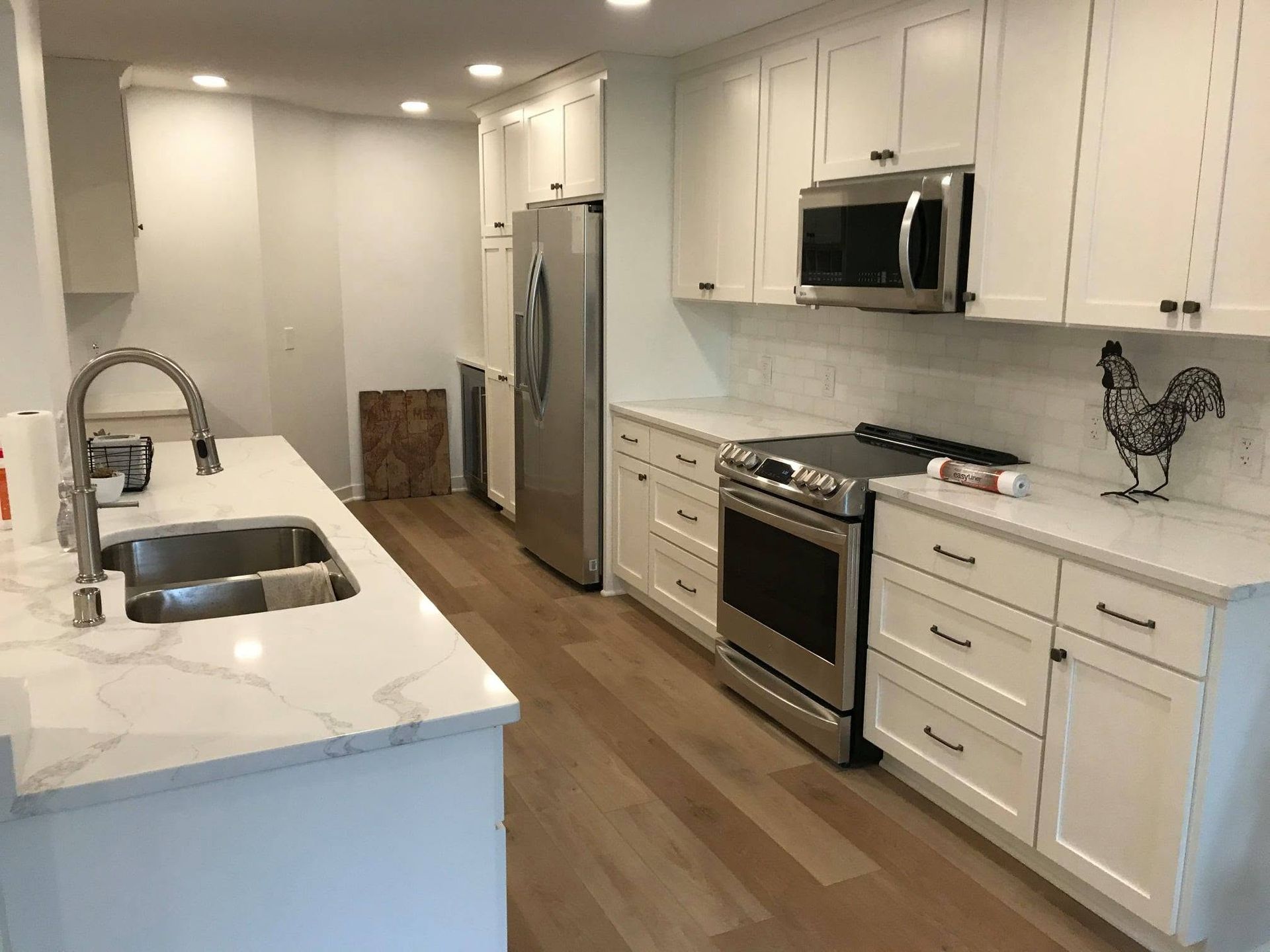 Modern white kitchen with marble island, stainless appliances, and wood floors