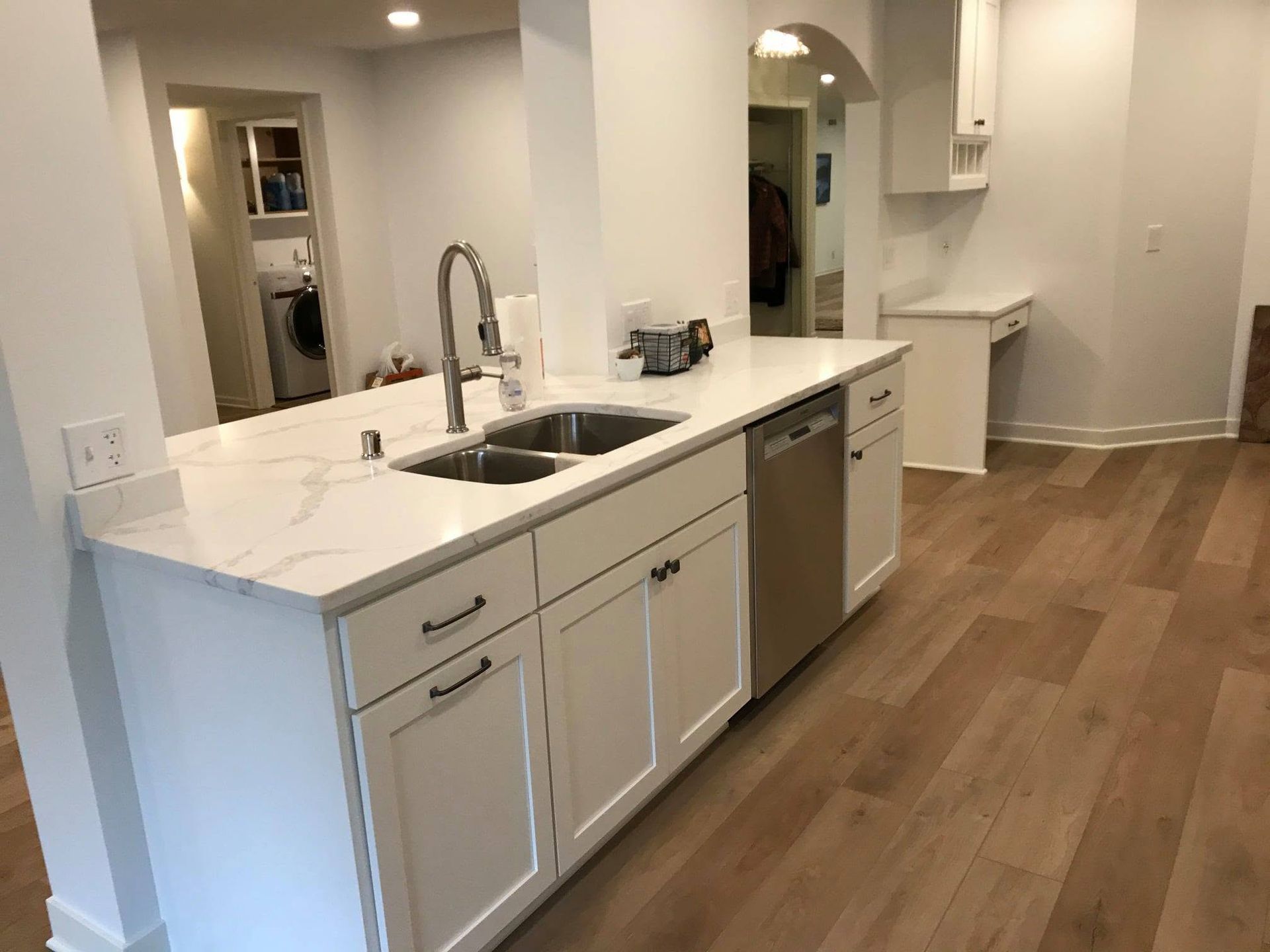 Bright modern kitchen with white cabinets, marble countertop, stainless sink, and wood floors