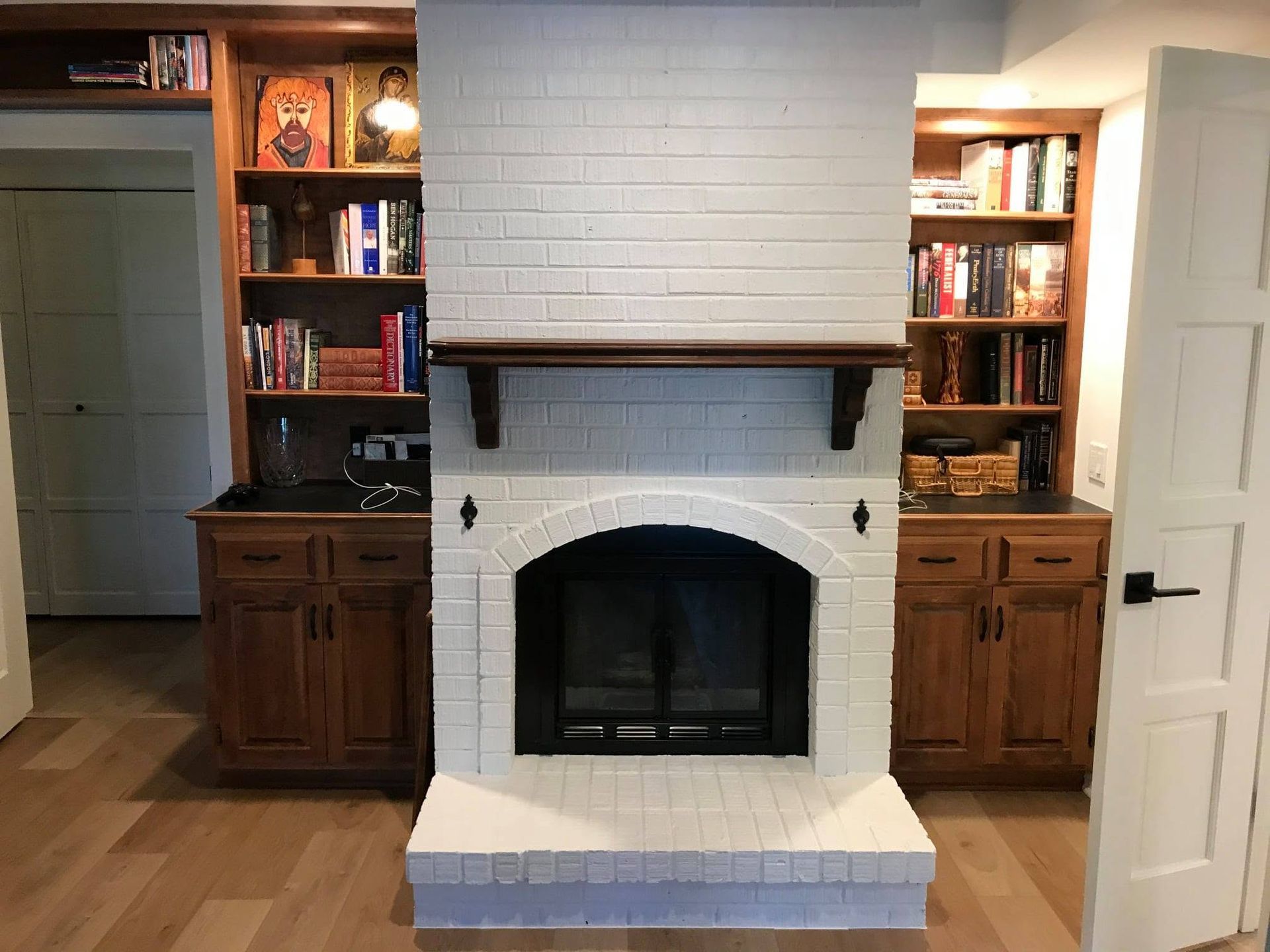 Built-in fireplace with white tile surround, wood mantle, and matching wood cabinets in a room.