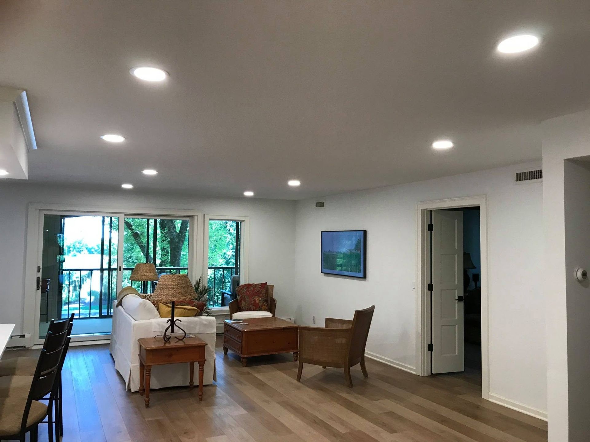 Bright open living room with sofa, chairs, dining table, and sliding glass doors to a balcony.