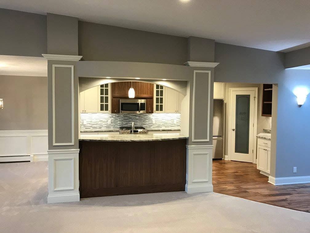 Empty room with a built-in wet bar, white columns, wood cabinet front, and tiled floor area