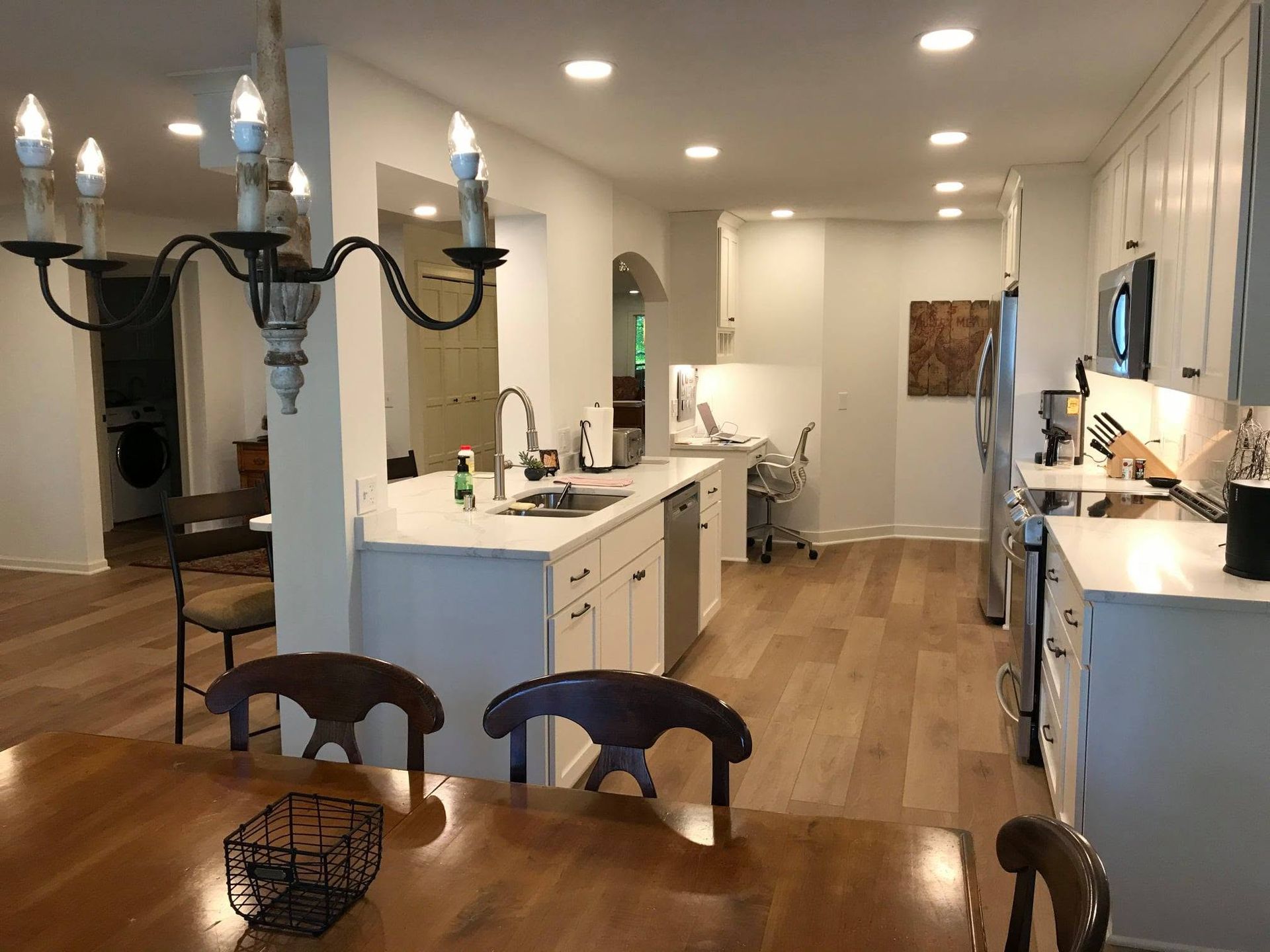 Bright modern kitchen with white cabinets, wood floors, island, and dining table in foreground