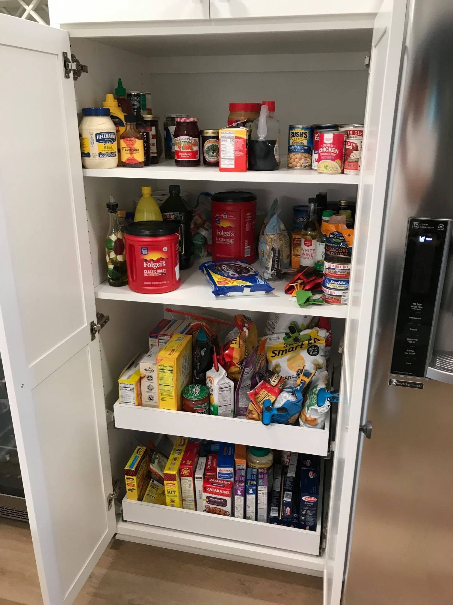 Open pantry cabinet stocked with assorted snacks, boxes, jars, and canned goods on three shelves.