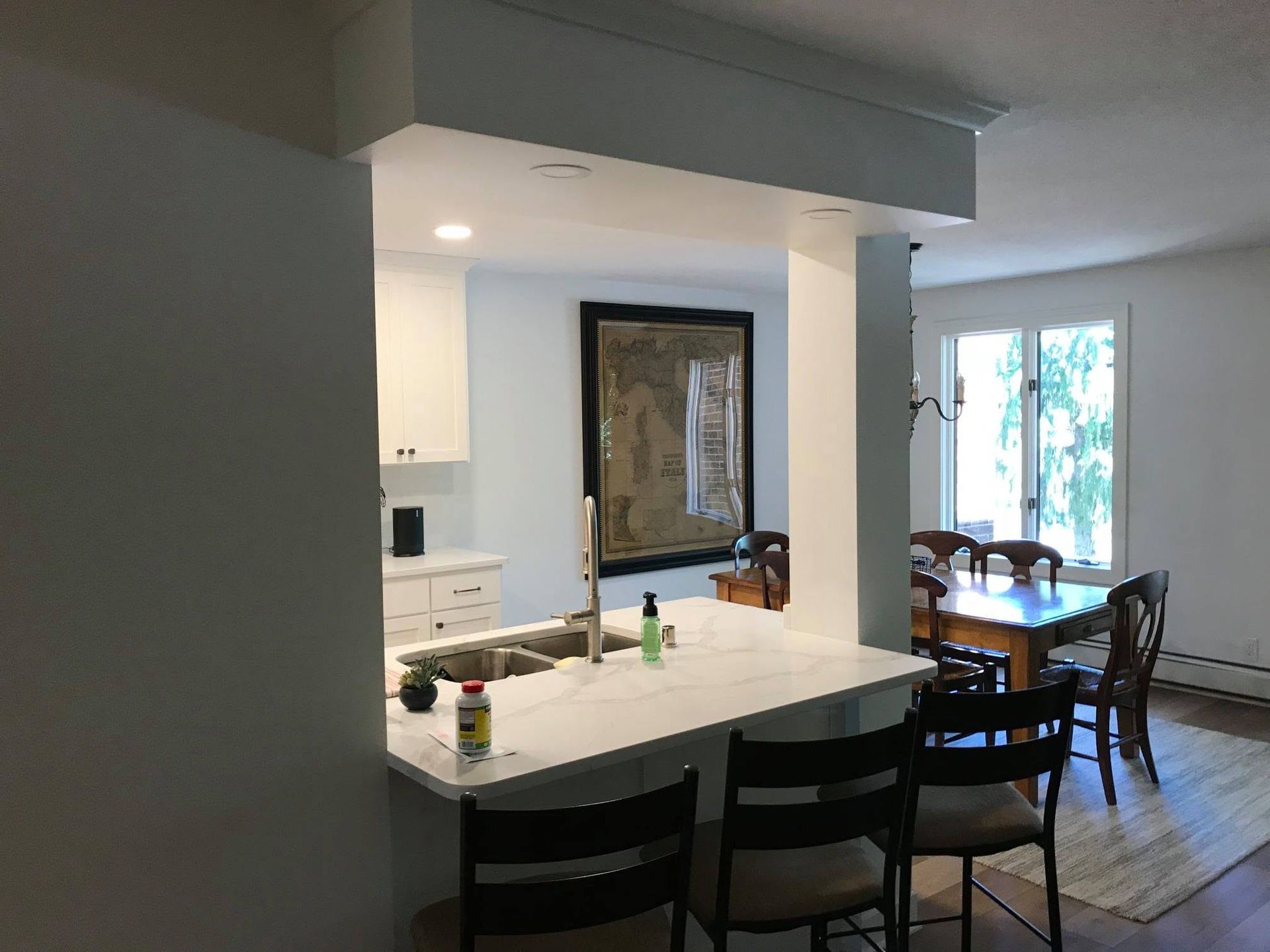 Modern kitchen with white island, black chairs, and dining table by a bright window