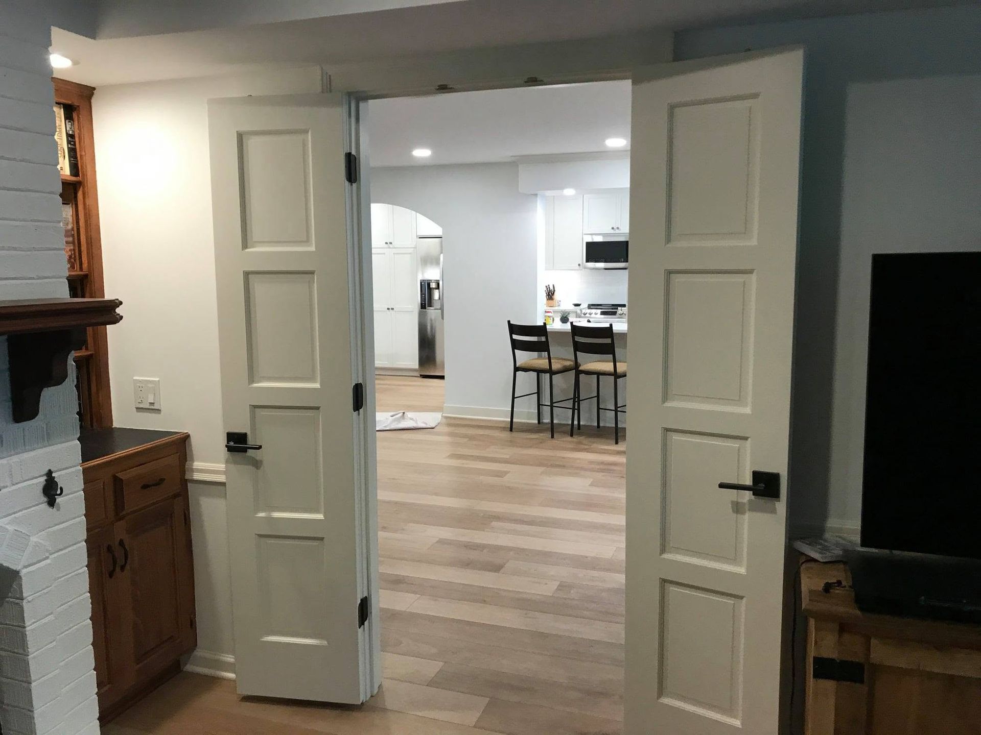 Open double doors to a bright kitchen with a wood floor and white cabinetry.