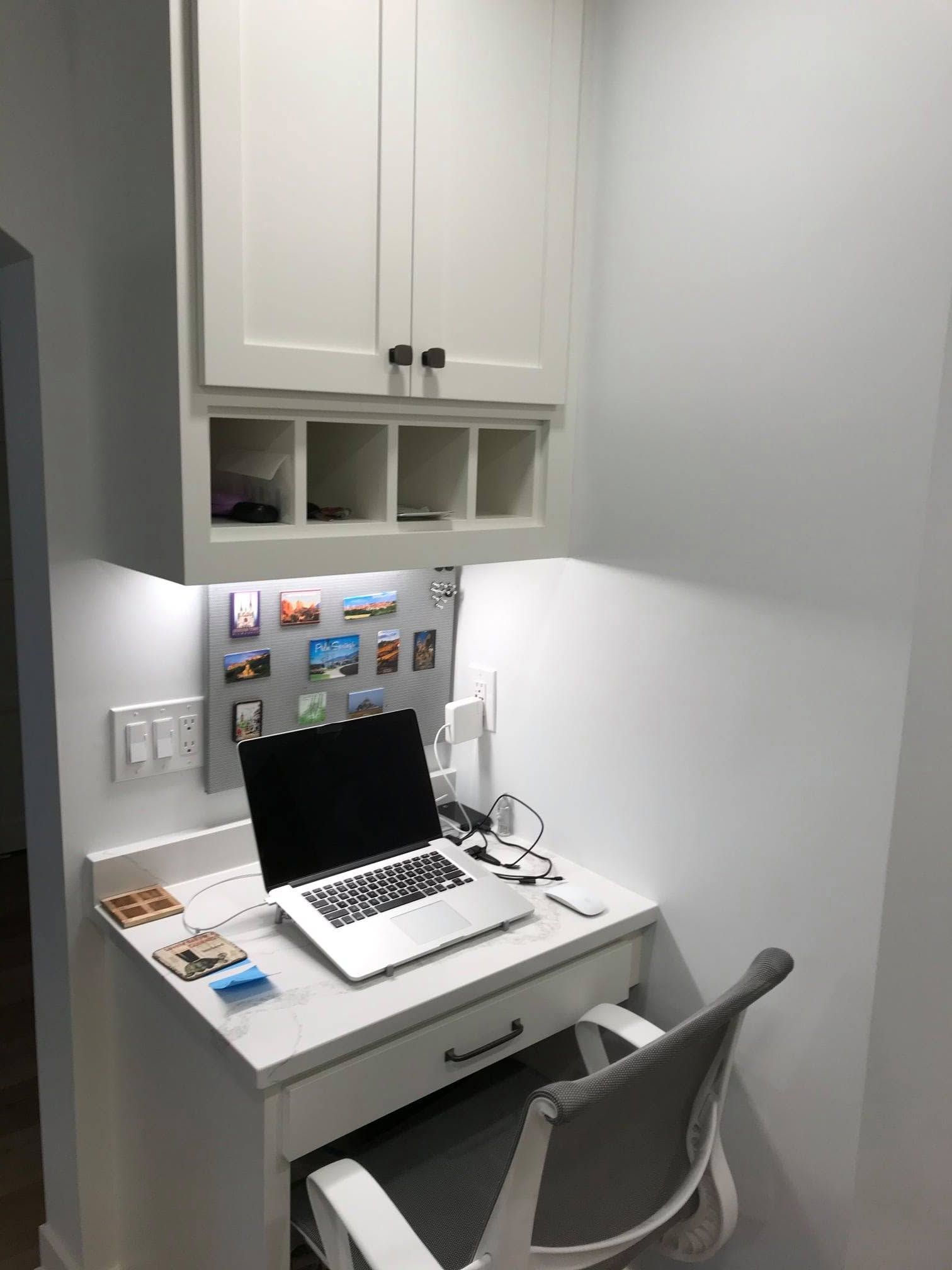 Small home office nook with a white desk, laptop, chair, and wall cabinets