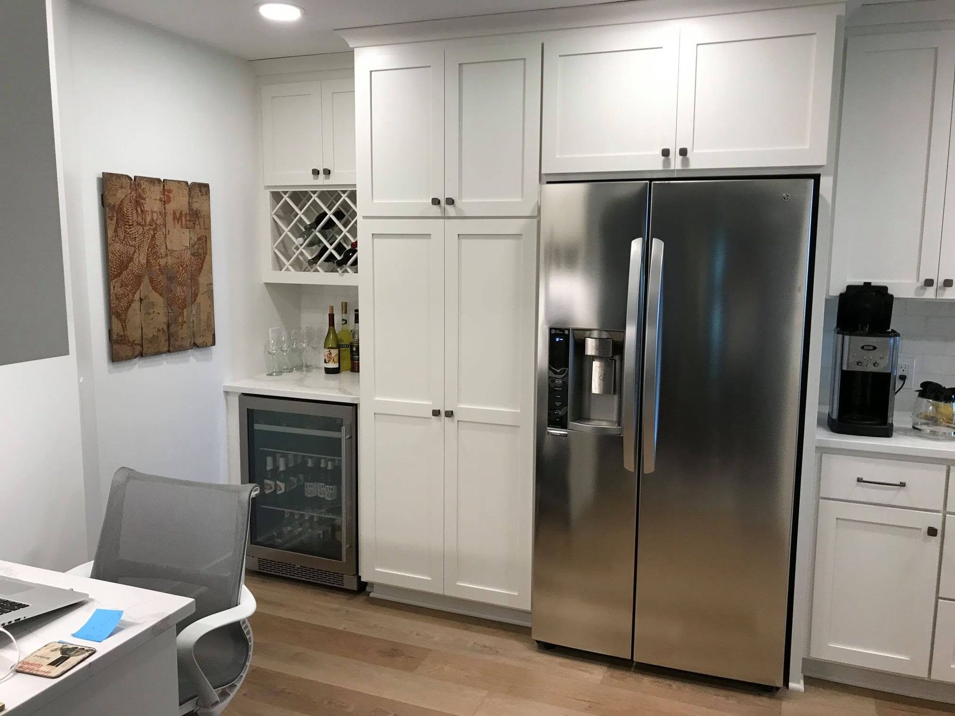 Modern kitchen with white cabinets, stainless steel refrigerator, and small dining area near a wine rack.