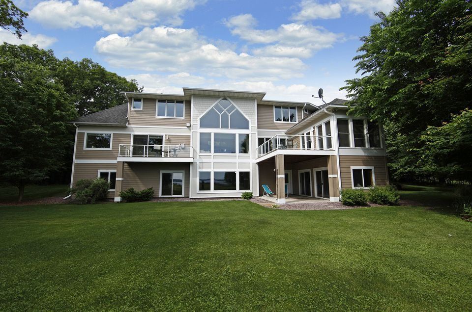 Large modern house with a glass-front entry and expansive green lawn under a partly cloudy sky