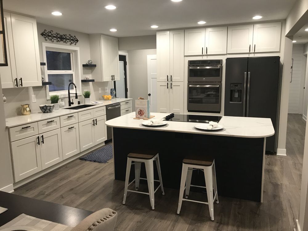 Modern white kitchen with black island, bar stools, and stainless steel appliances
