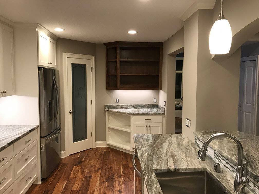Modern kitchen with white cabinets, stainless fridge, dark wood floor, and granite countertops