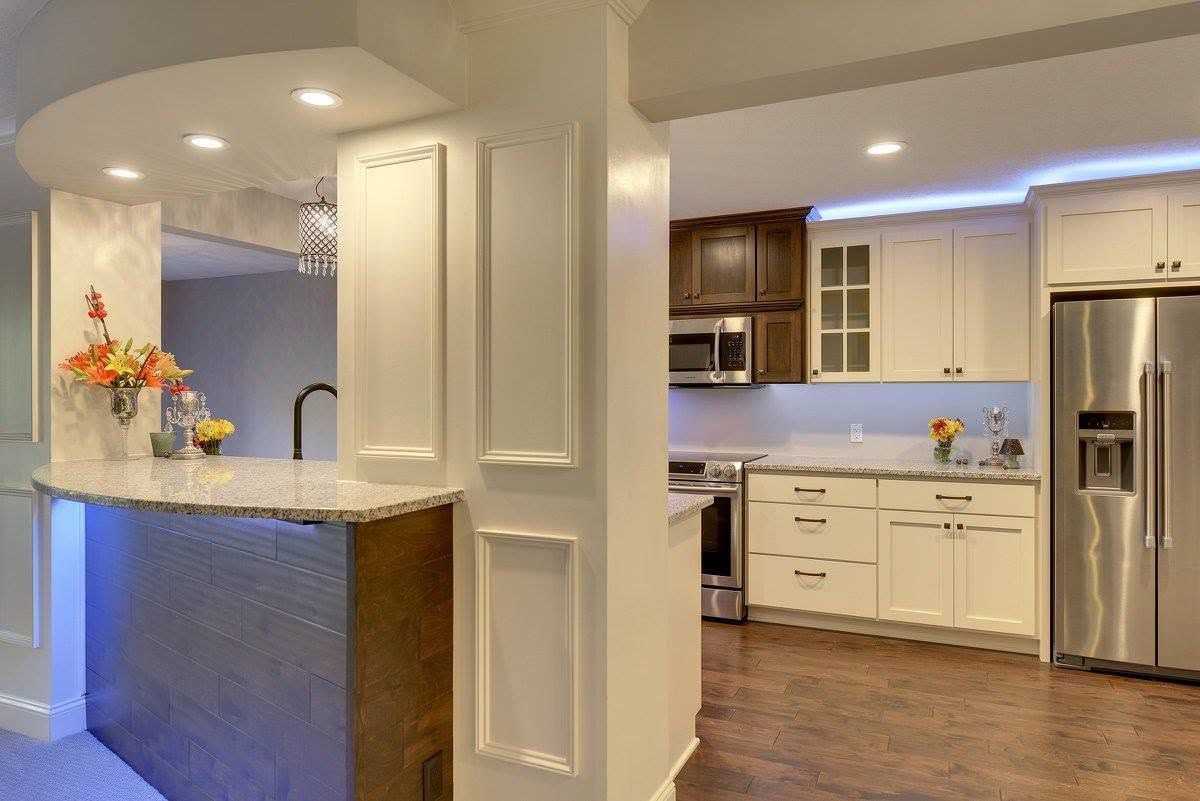 Bright kitchen with white cabinets, granite bar, stainless fridge, and blue accent lighting over wood floors