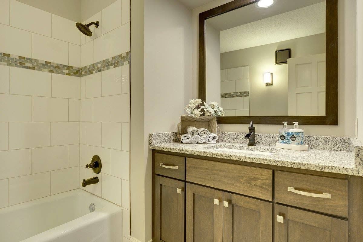 Bathroom vanity with granite countertop, mirror, sink, and bathtub with tiled shower wall