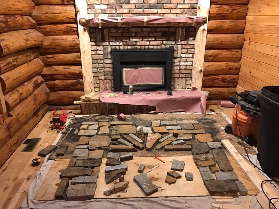 Stone slab layout on a wooden table in a log cabin before a brick fireplace and stove area