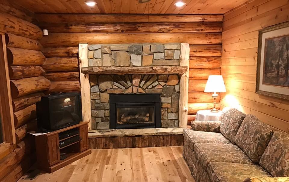 Cozy log cabin living room with stone fireplace, TV, couch, and lamp in warm wood-paneled interior