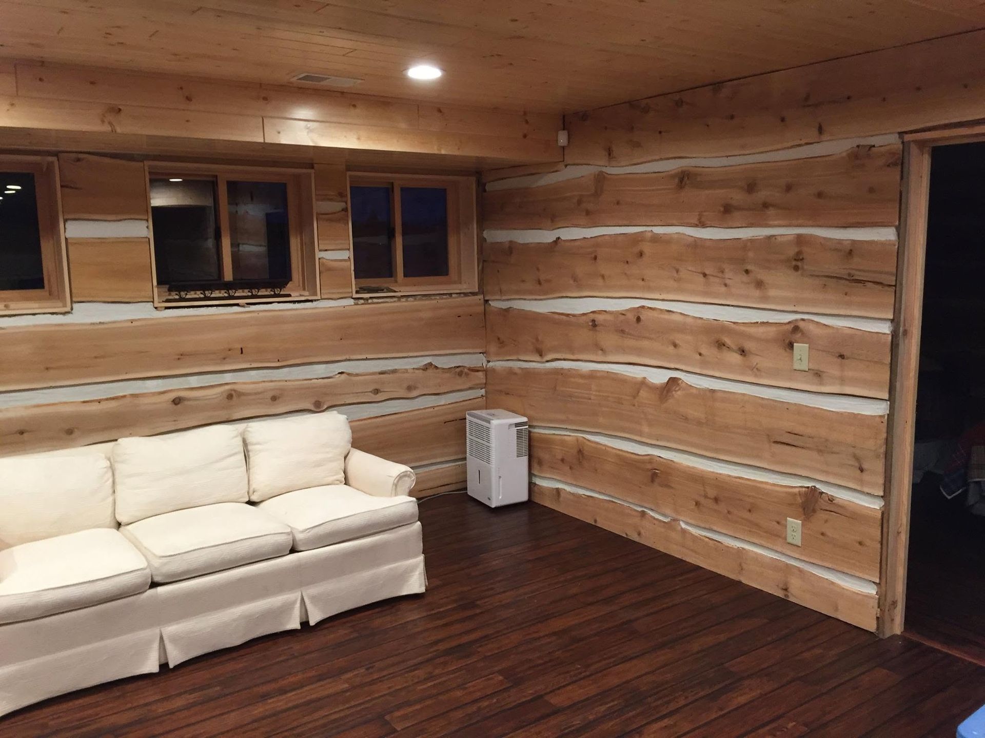 Cozy log cabin living room with white sofa, wood-paneled walls, and dark hardwood floor