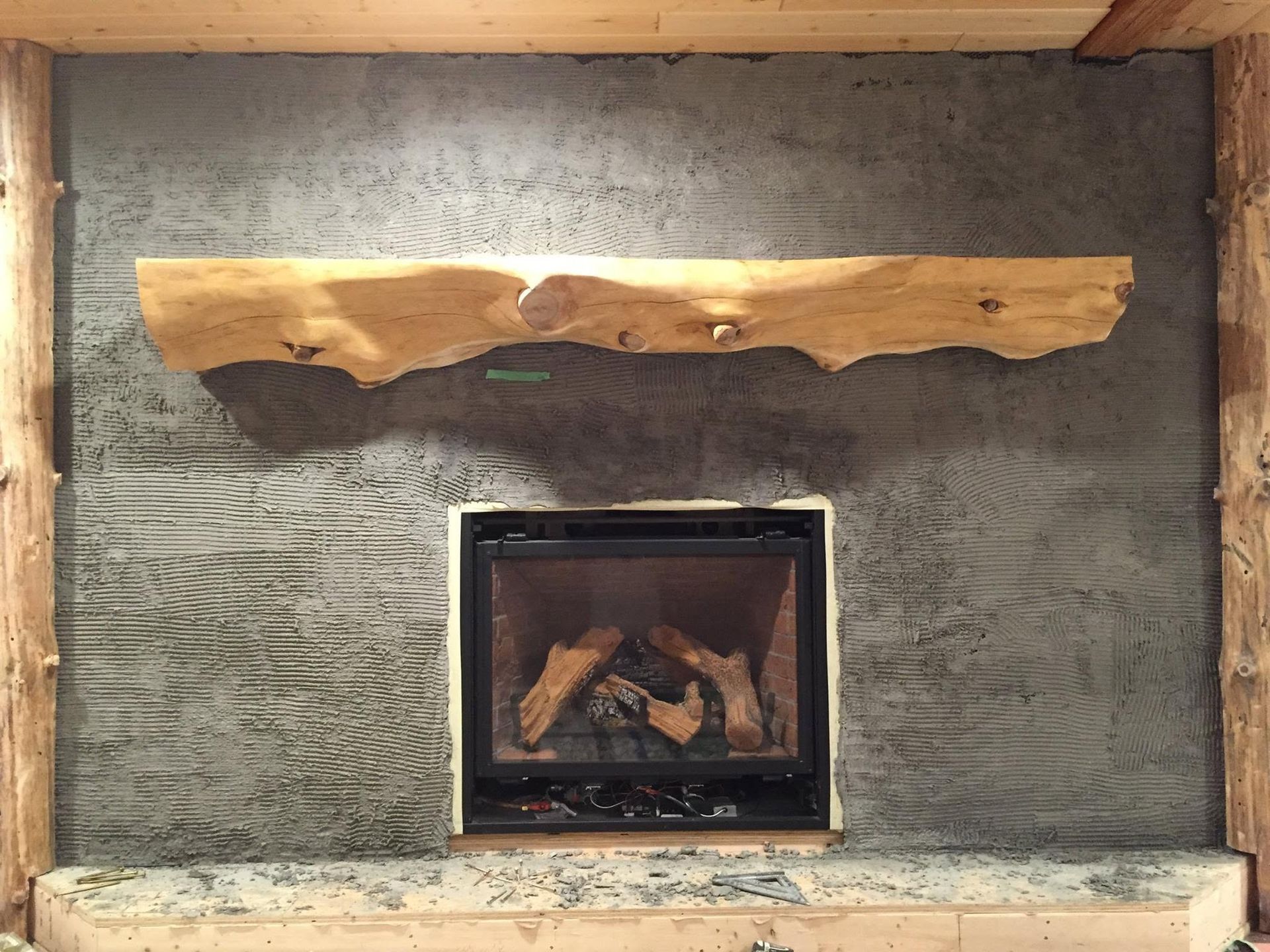 Stone fireplace with a small glass-front firebox and a rustic wooden mantel shelf above.