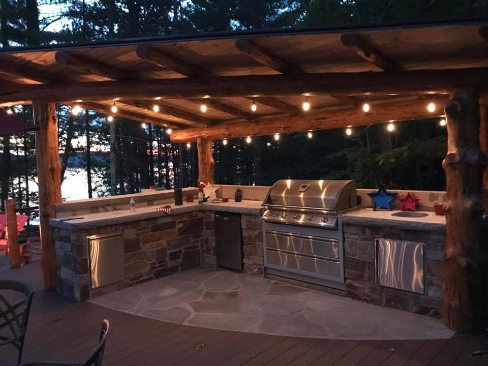 Outdoor covered kitchen with stone counter, built-in grill, and string lights at dusk