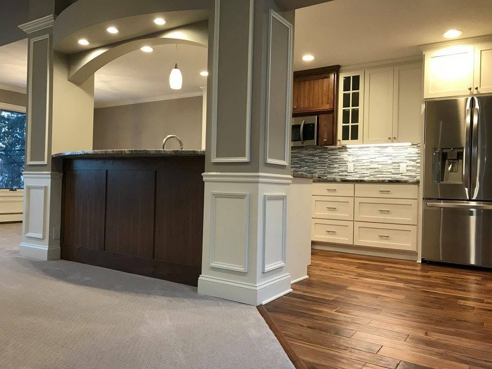 Open-plan kitchen with dark island, white cabinets, stainless fridge, and wood flooring