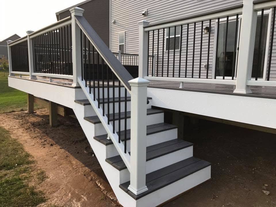 Raised deck staircase with black railings and white trim beside a house