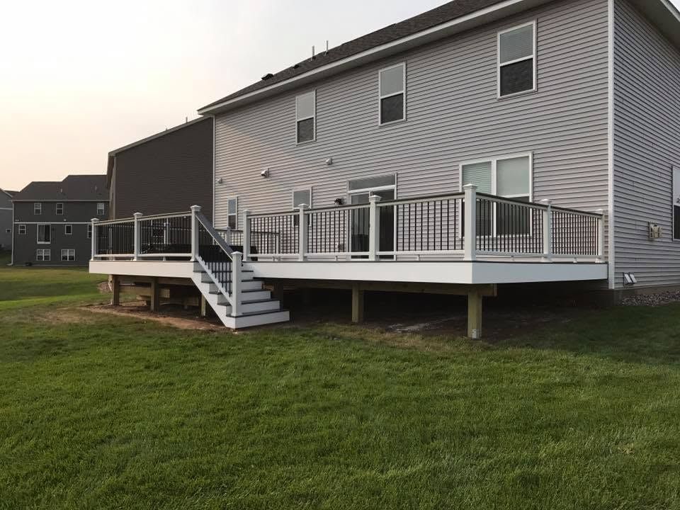 Raised backyard deck with stairs attached to a gray house over a grassy lawn.
