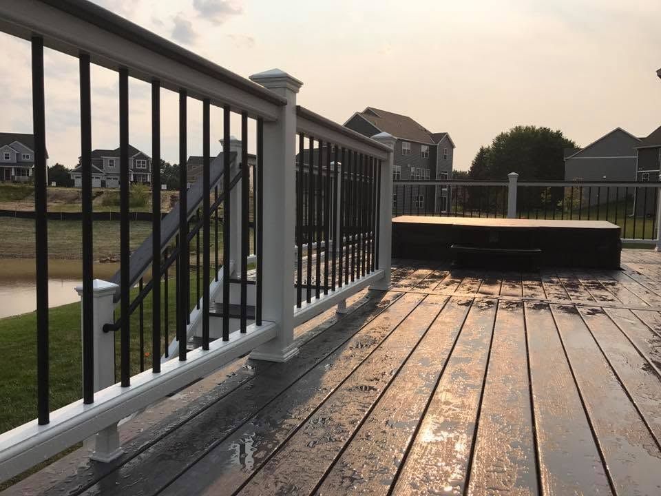 Wet wooden deck with black railing overlooking a suburban backyard at sunset