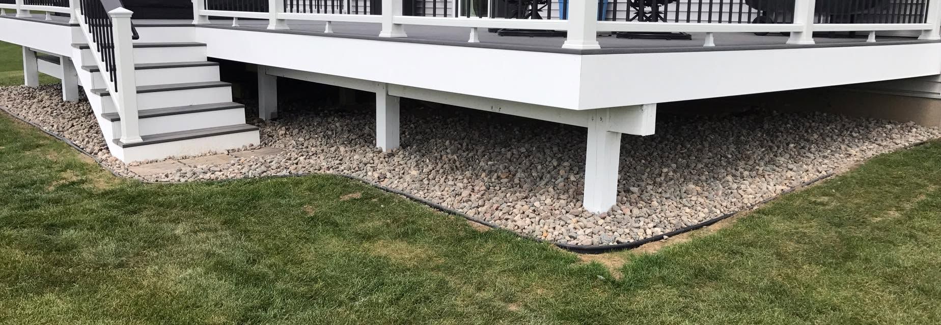 White raised deck with stairs, white railing, and gravel border beside a green lawn.