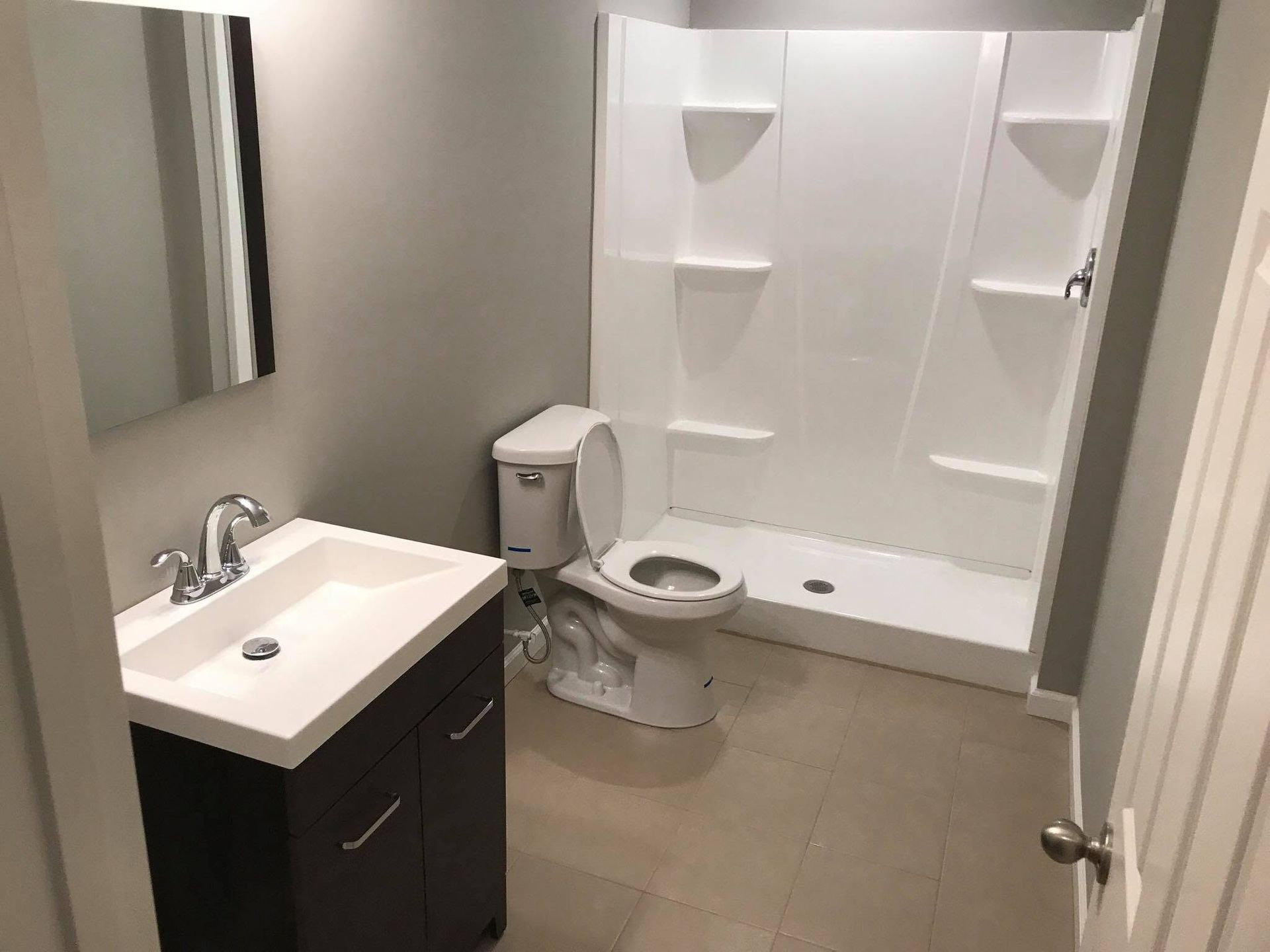 Small accessible bathroom with sink, toilet, mirror, and walk-in shower area with built-in shelves.