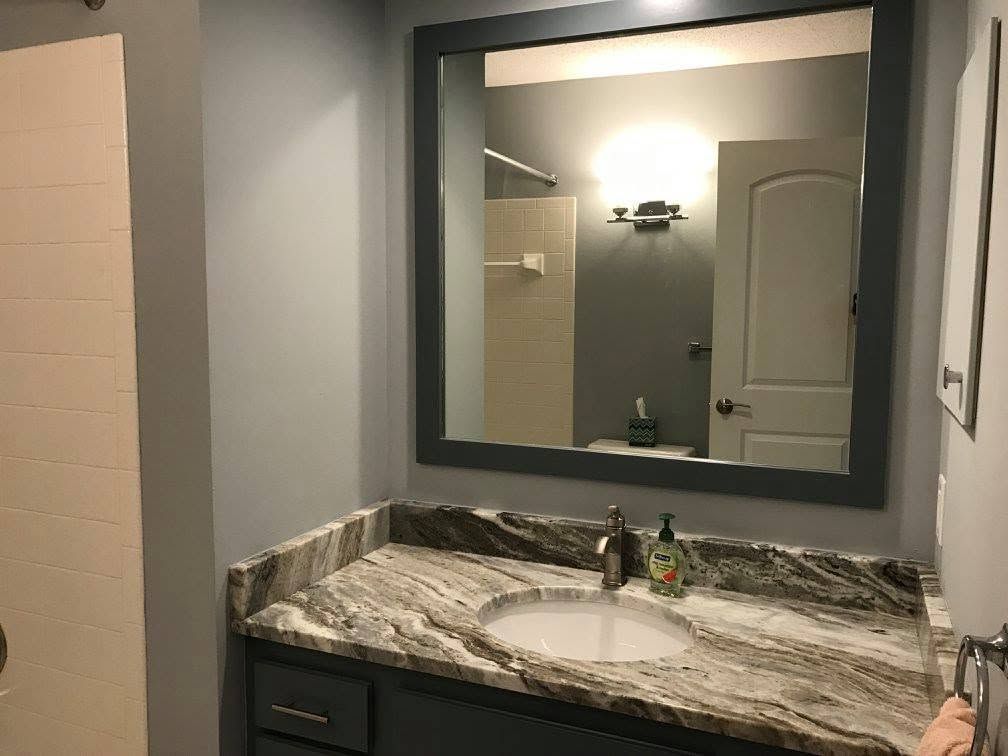 Bathroom vanity with granite countertop, large mirror, and sink beneath a wall light.