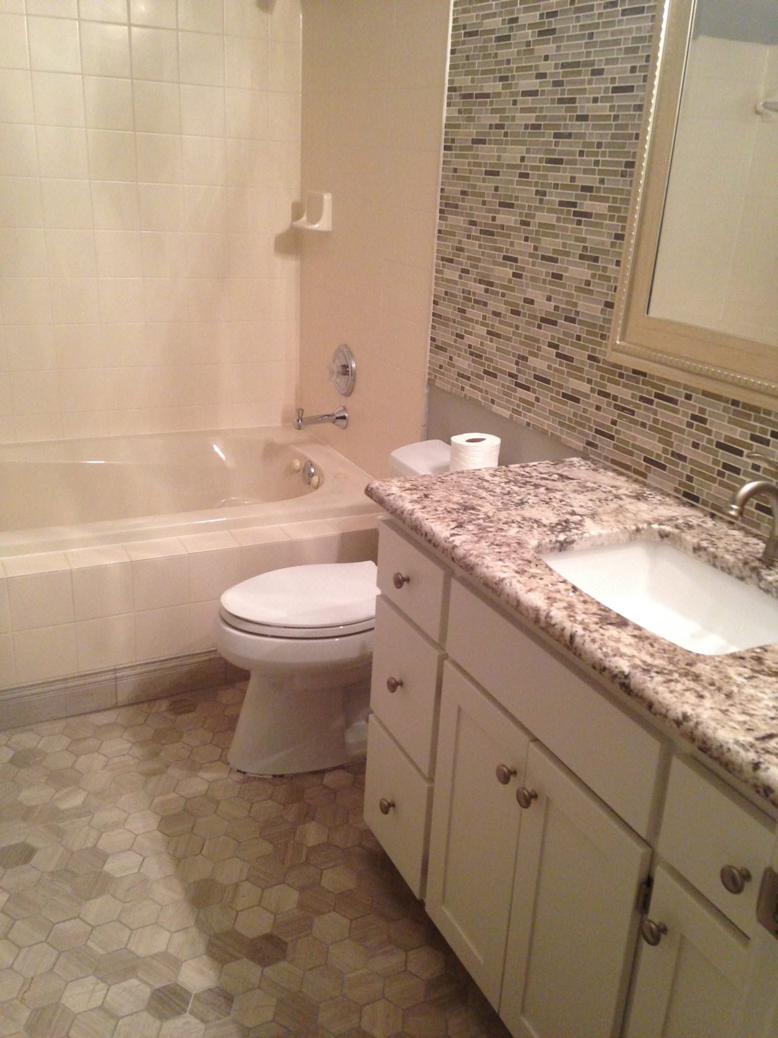 Bathroom with tub, toilet, and granite vanity with sink and mosaic tile backsplash.