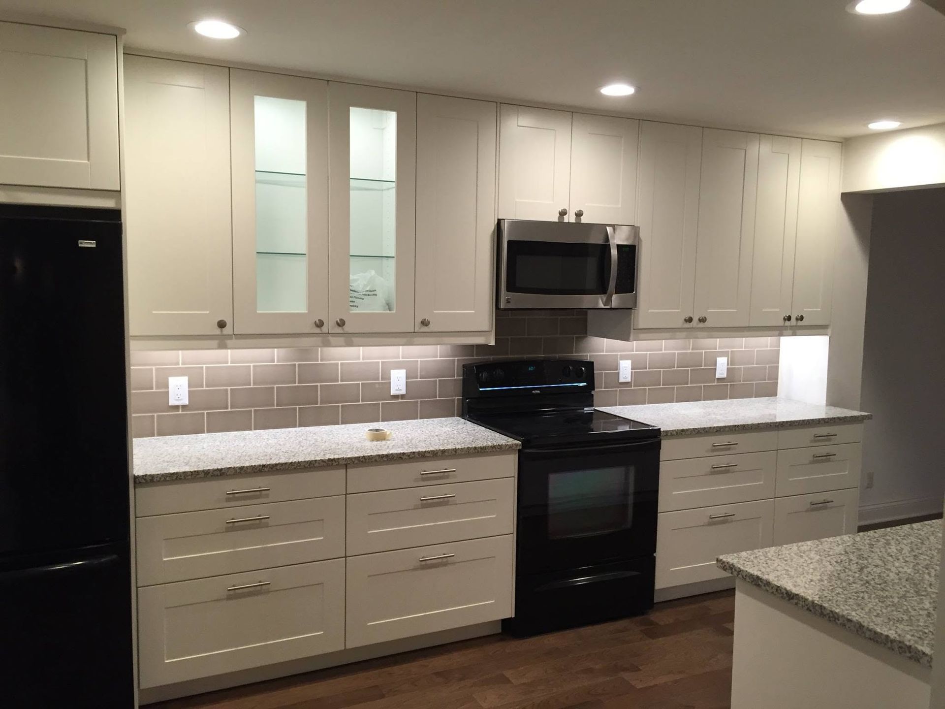 Modern kitchen with white cabinets, black appliances, granite countertops, and beige tile backsplash.
