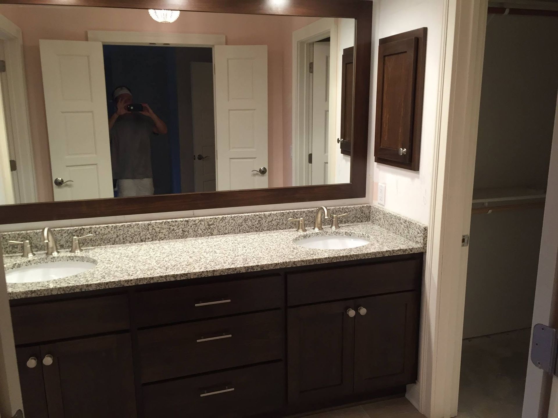Bathroom vanity with granite countertop, large mirror, and dark wood cabinets reflecting a person taking the photo