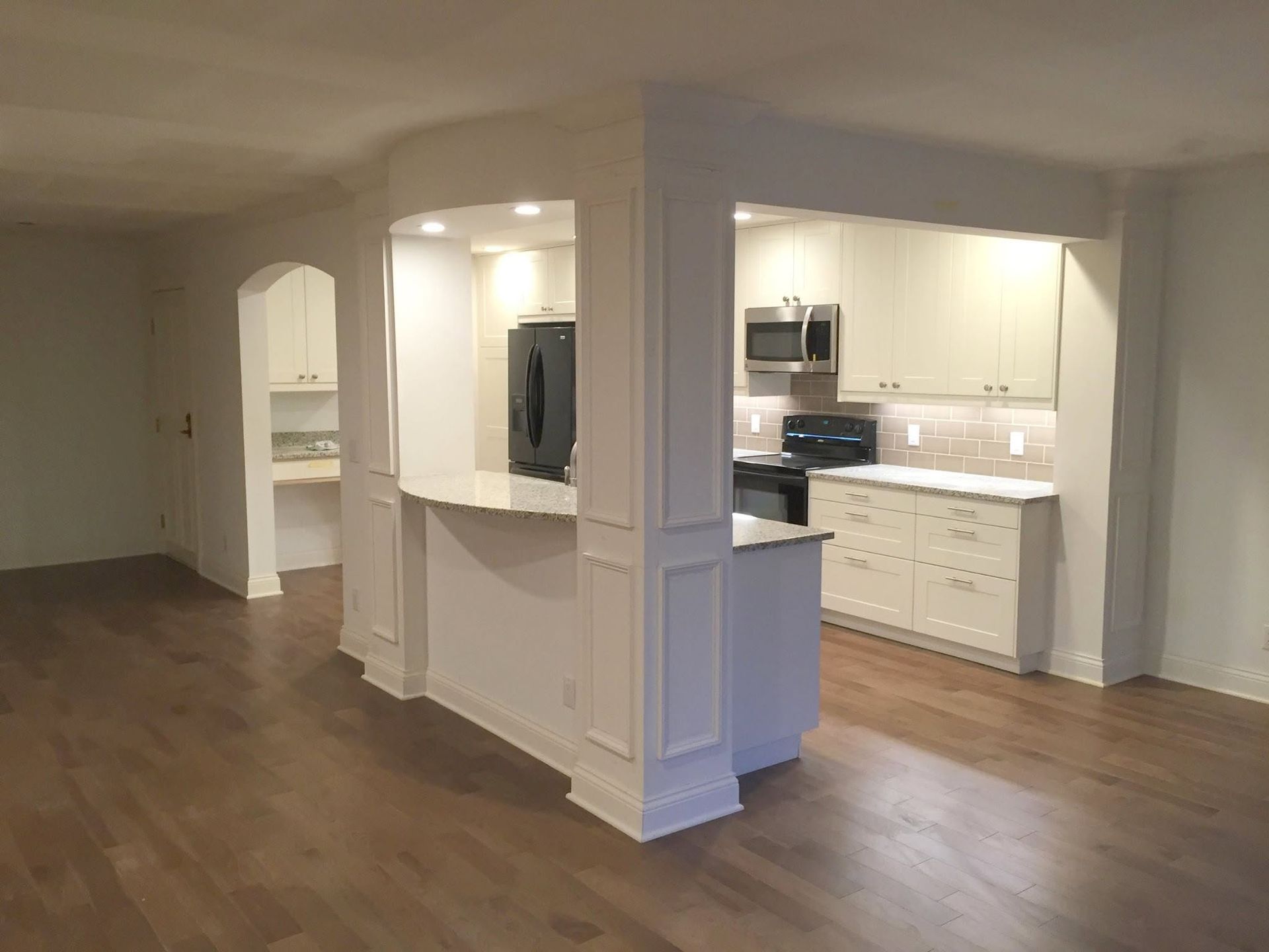 Empty open-plan apartment with wood floors, white walls, and a kitchen bar area