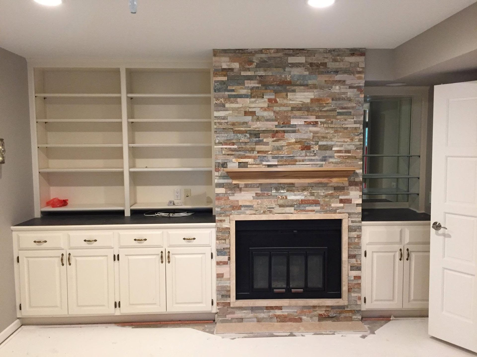 Living room with built-in white cabinets, open shelves, and a stone fireplace with a glass insert.