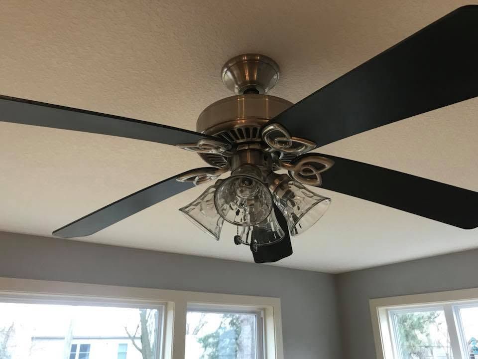 Ceiling fan with black blades and chandelier light in a bright room with windows