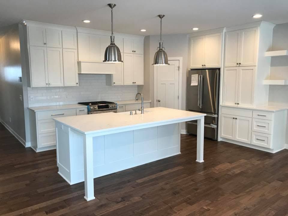 Bright white kitchen with island, stainless fridge, pendant lights, and dark hardwood floors