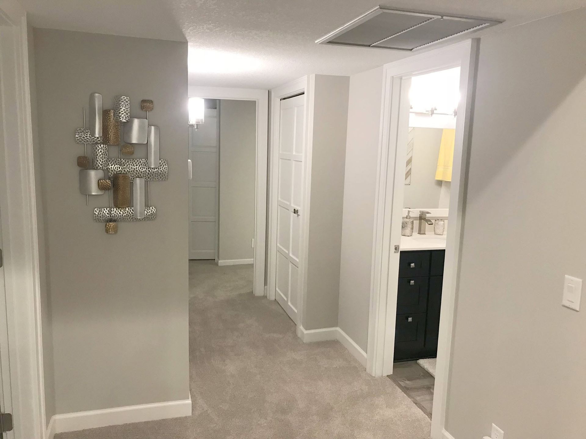 Hallway with gray carpet, white doors, and a bathroom vanity visible through an open doorway.