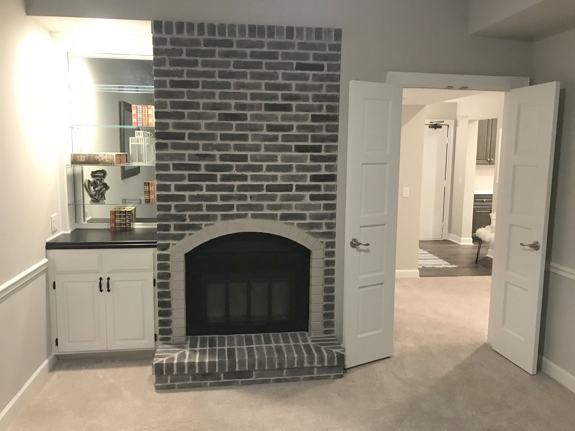 Living room with a brick fireplace, white cabinets, and open double doors to another room