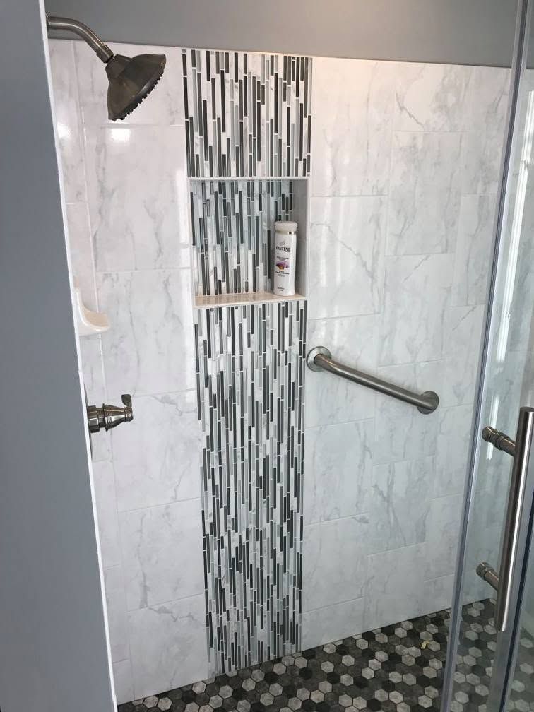 Small shower stall with white tile, gray mosaic accent strip, and metal grab bars.