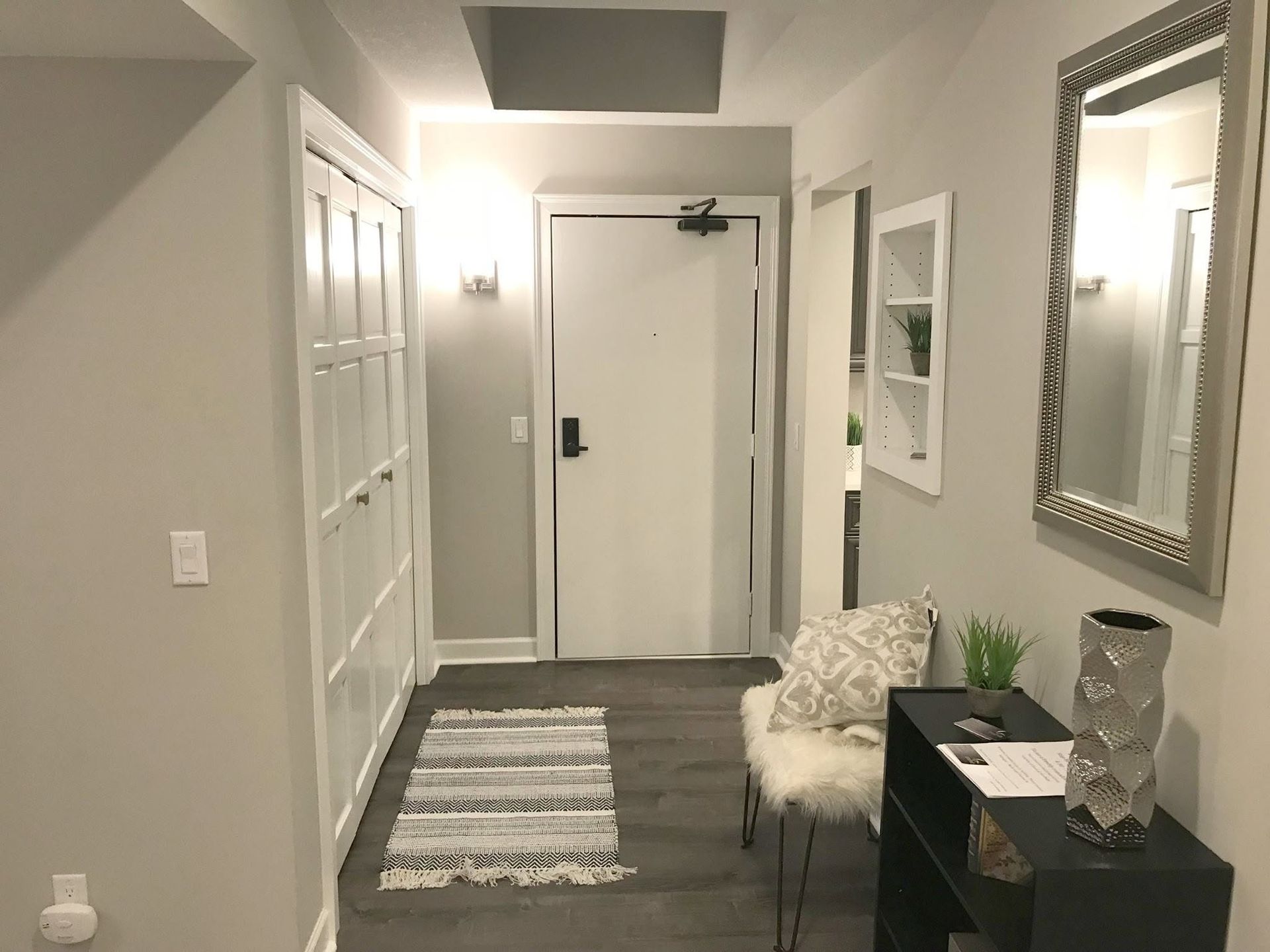 Narrow hallway with white doors, gray rug, console table, mirror, and a lit ceiling in modern decor.