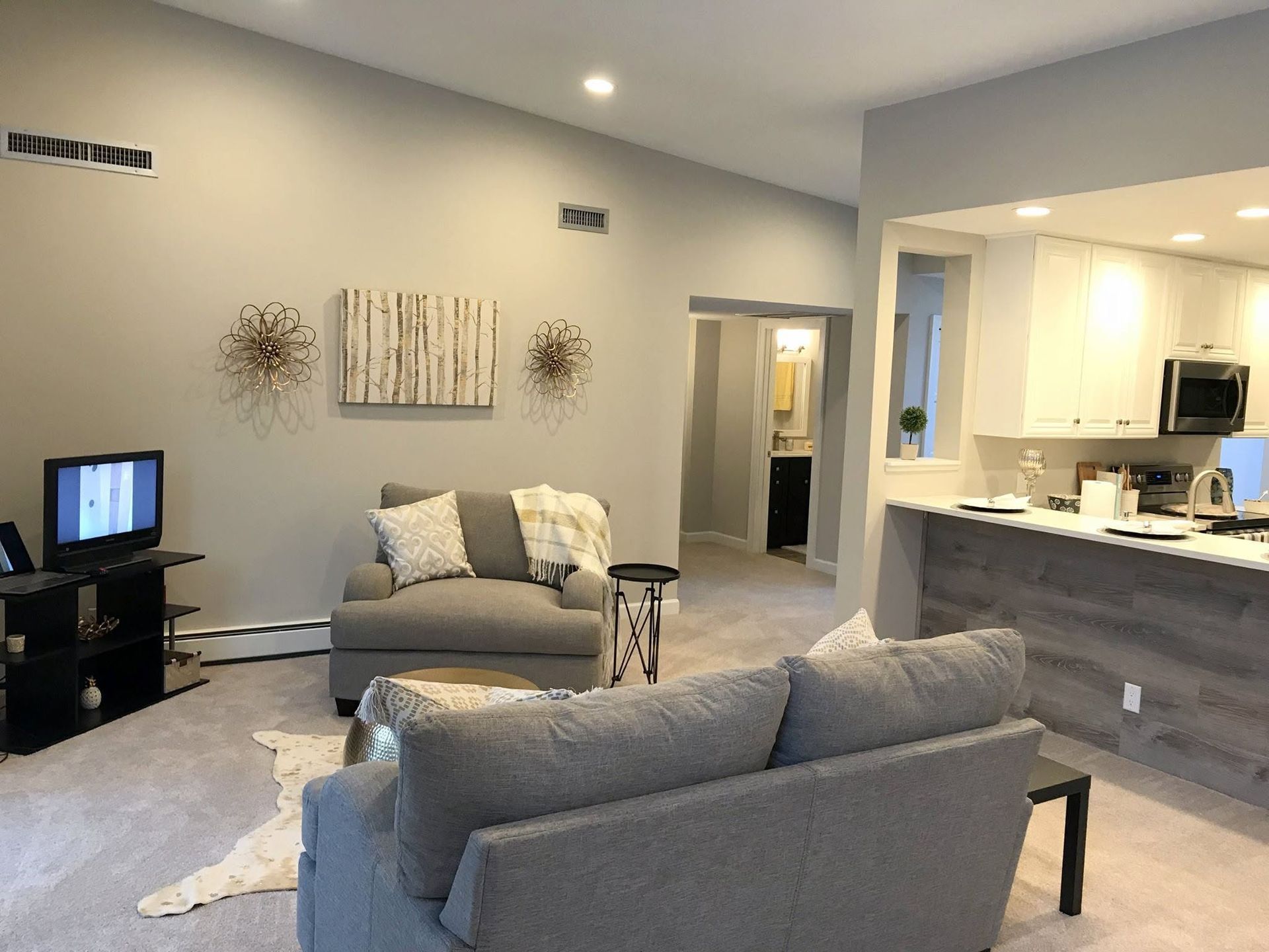 Modern living room with gray sofas, wall art, and an open kitchen area