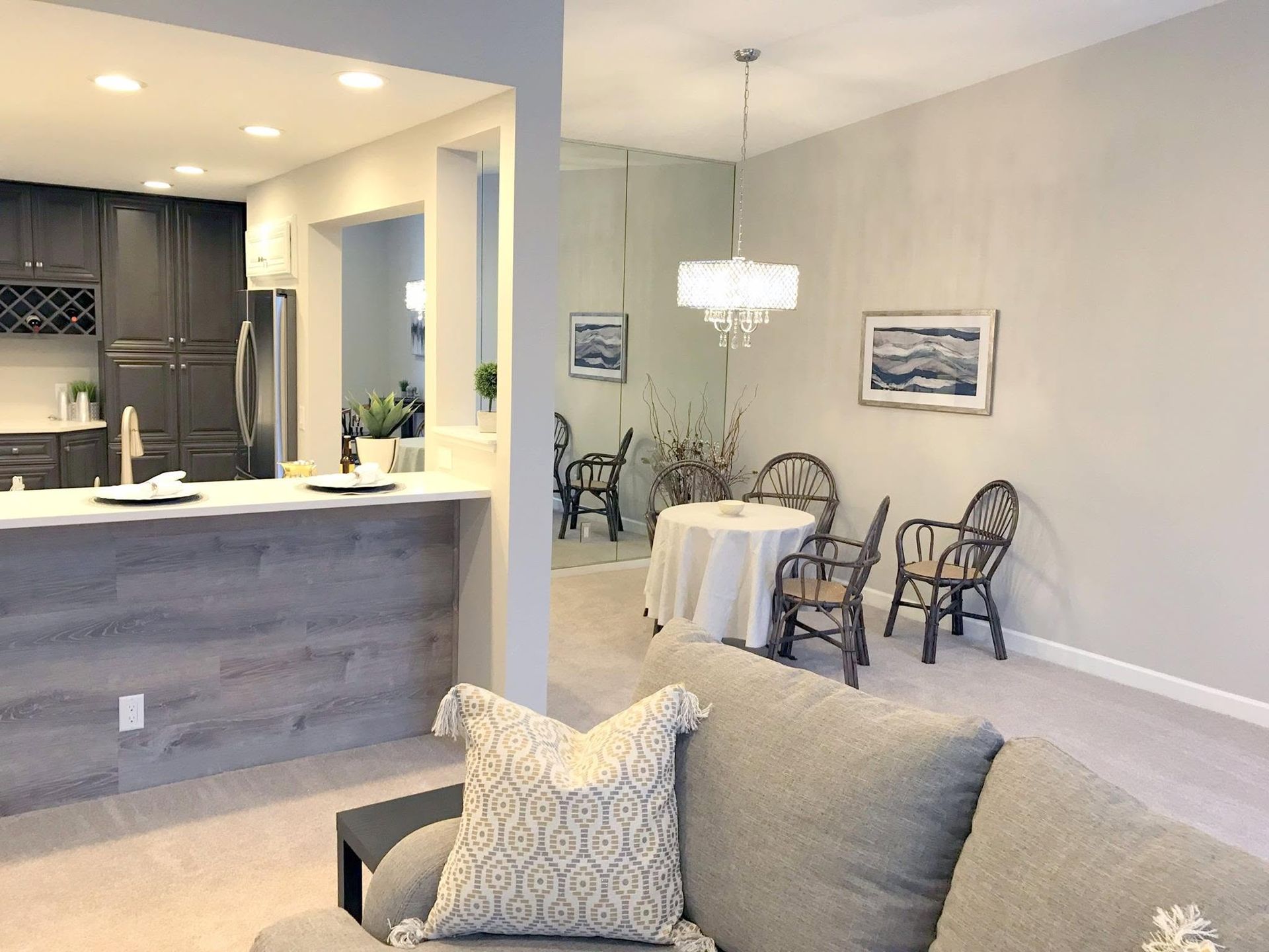 Open-plan living and dining area with kitchen bar, gray sofa, and table with white chairs