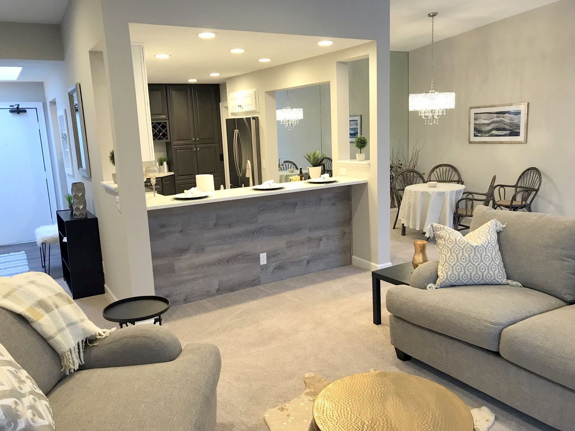 Open-concept living room with gray sofa, beige carpet, and a kitchen pass-through in the background