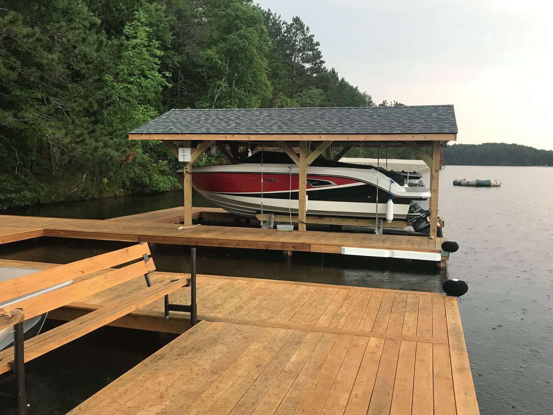 Wooden dock beside a lake, with covered boat lift and red canoe under a shingled roof.