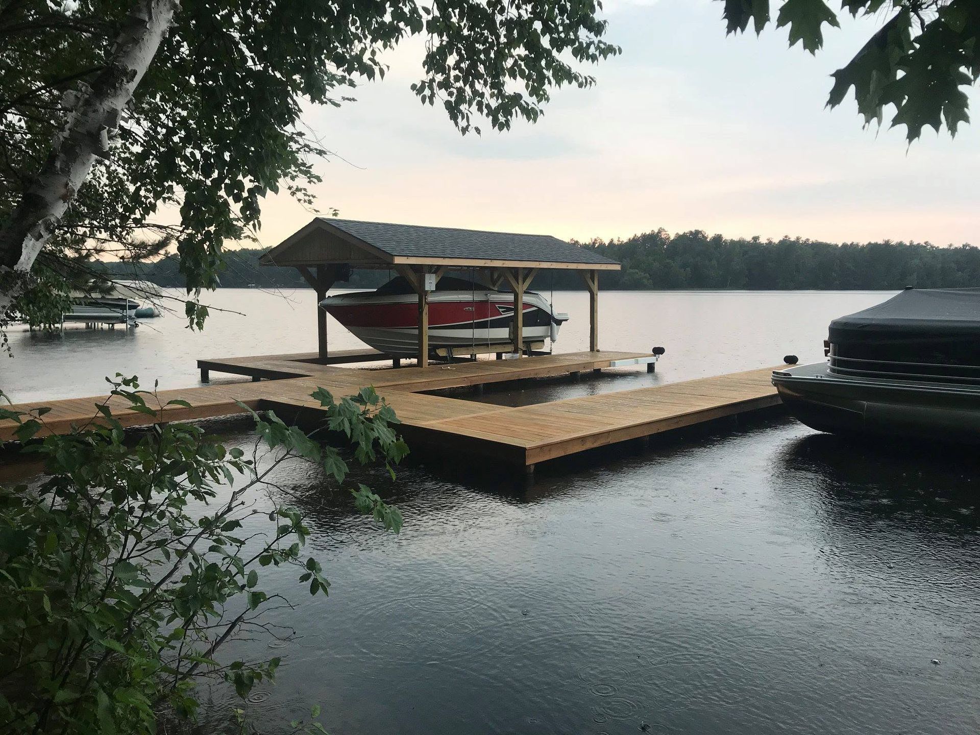 Lakeside dock with covered boat slips at sunset, framed by overhanging trees and calm water.