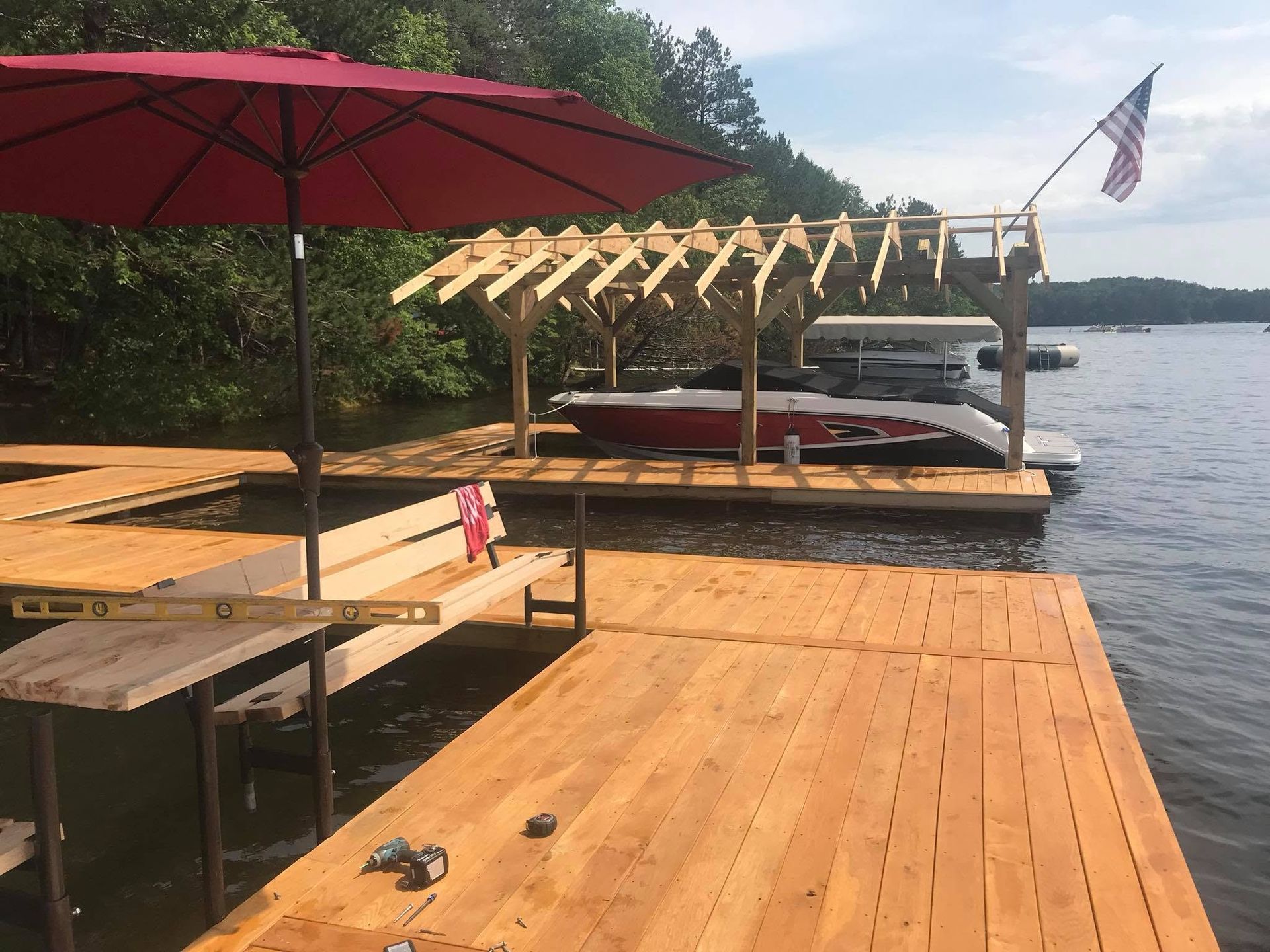 Wooden lakeside dock with red umbrella, boat lift, and American flag on a sunny day